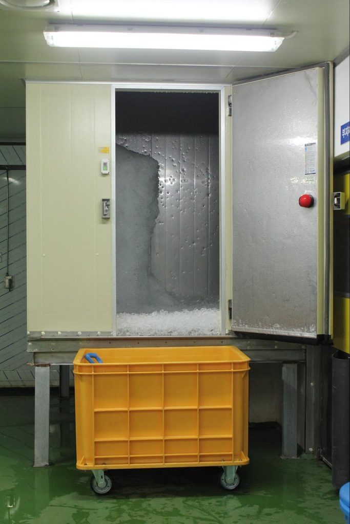 Industrial freezing equipment with an open insulated door and a yellow plastic container at Samsam Mulsan's seafood processing facility.
